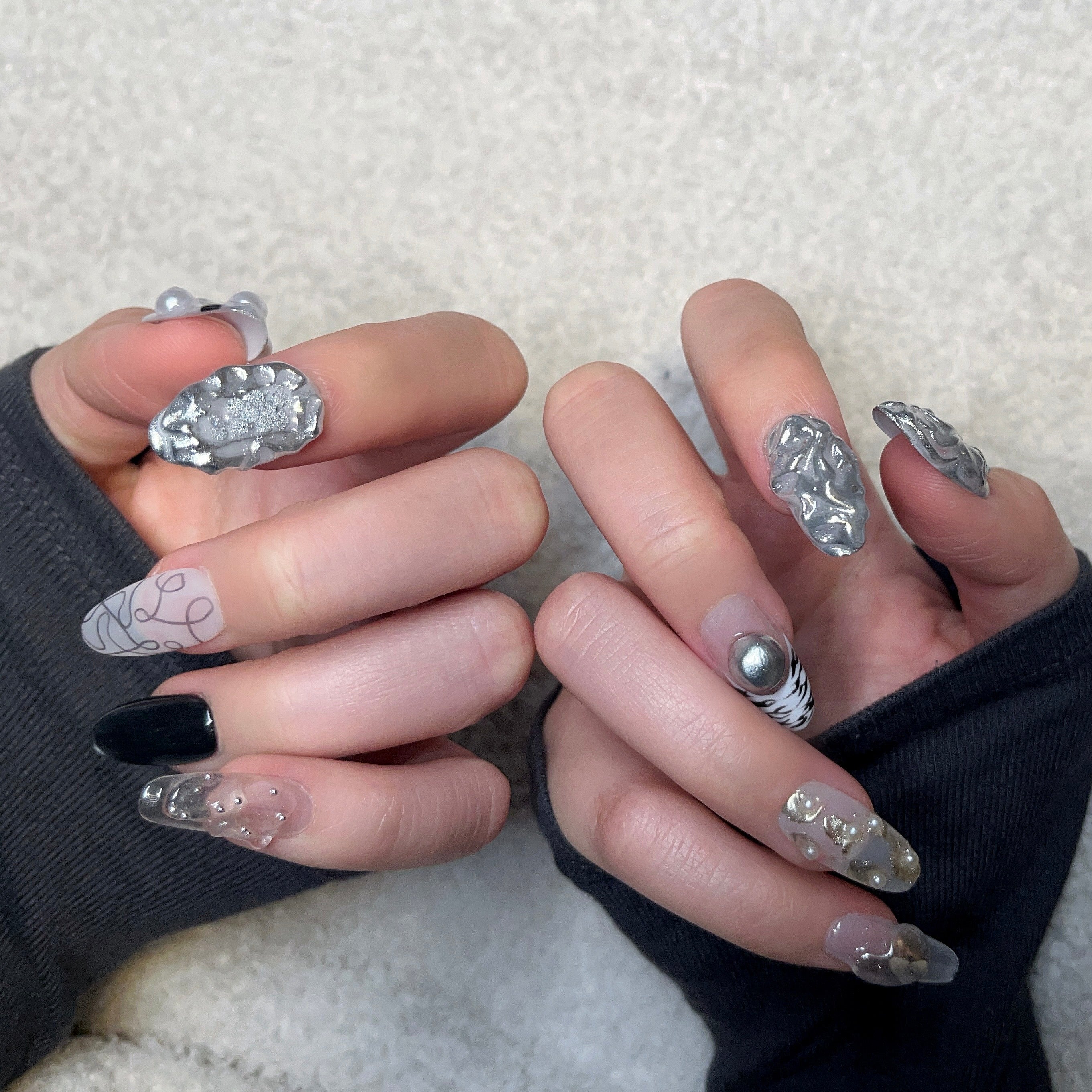 Handmade silver 3D almond press-on nails from Fjaka Nails, second hand model wear shot showcasing raised silver texture, pearls, steel beads, clear base, zebra print, cat eye and abstract swirl designs, salon-quality reusable nails for UK niche industrial aesthetic lovers