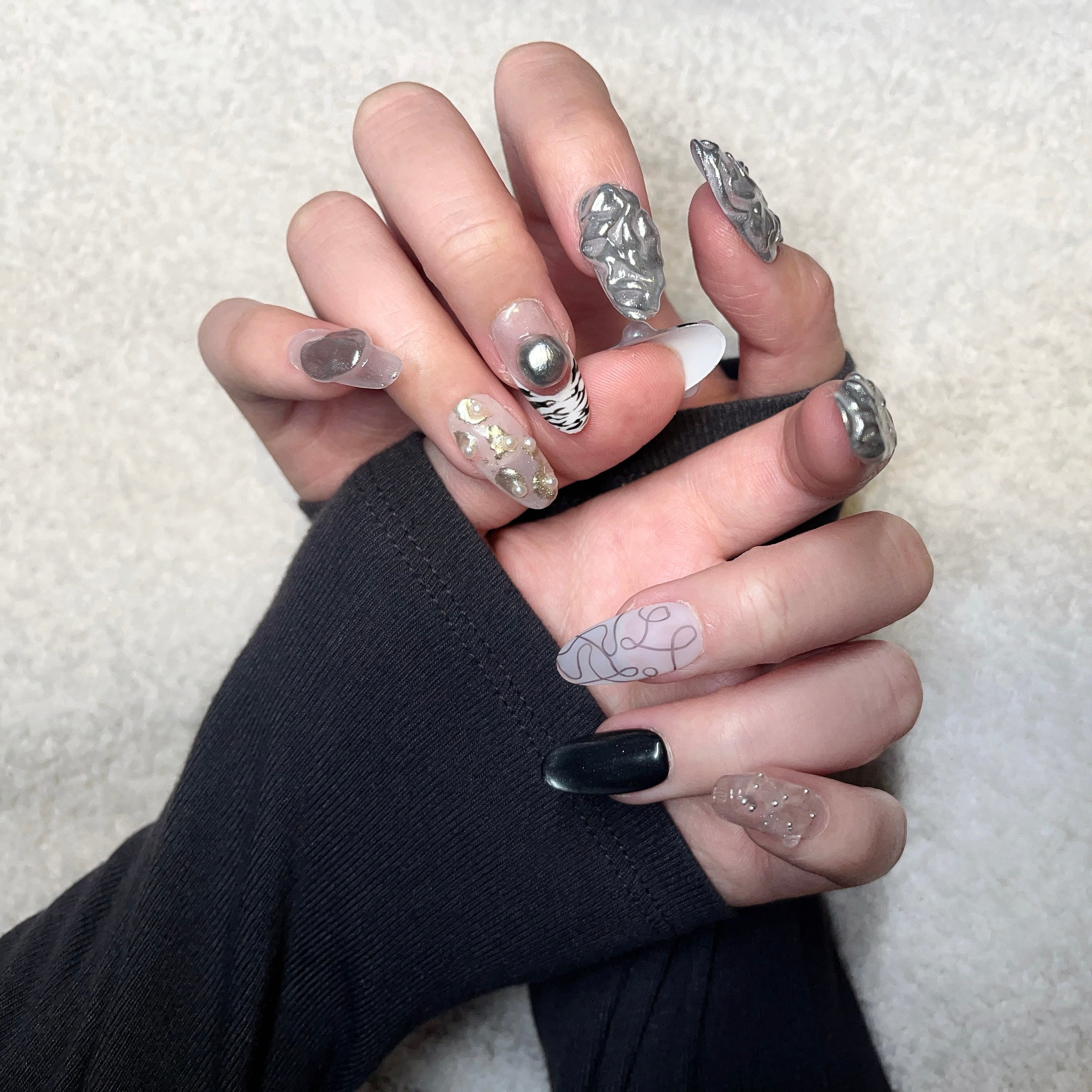 Handmade silver 3D almond press-on nails from Fjaka Nails, hand model wear shot showcasing raised silver texture, pearls, steel beads, clear base, zebra print, cat eye and abstract designs, salon-quality reusable nails for UK niche industrial aesthetic lovers.